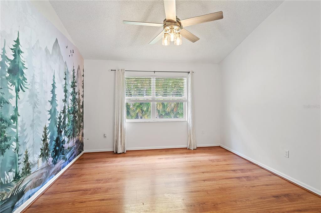 An empty bedroom features wood-look flooring, a ceiling fan, and a mountain-themed mural wall — 5647 MONTE ROSSO ROAD, SARASOTA, FL