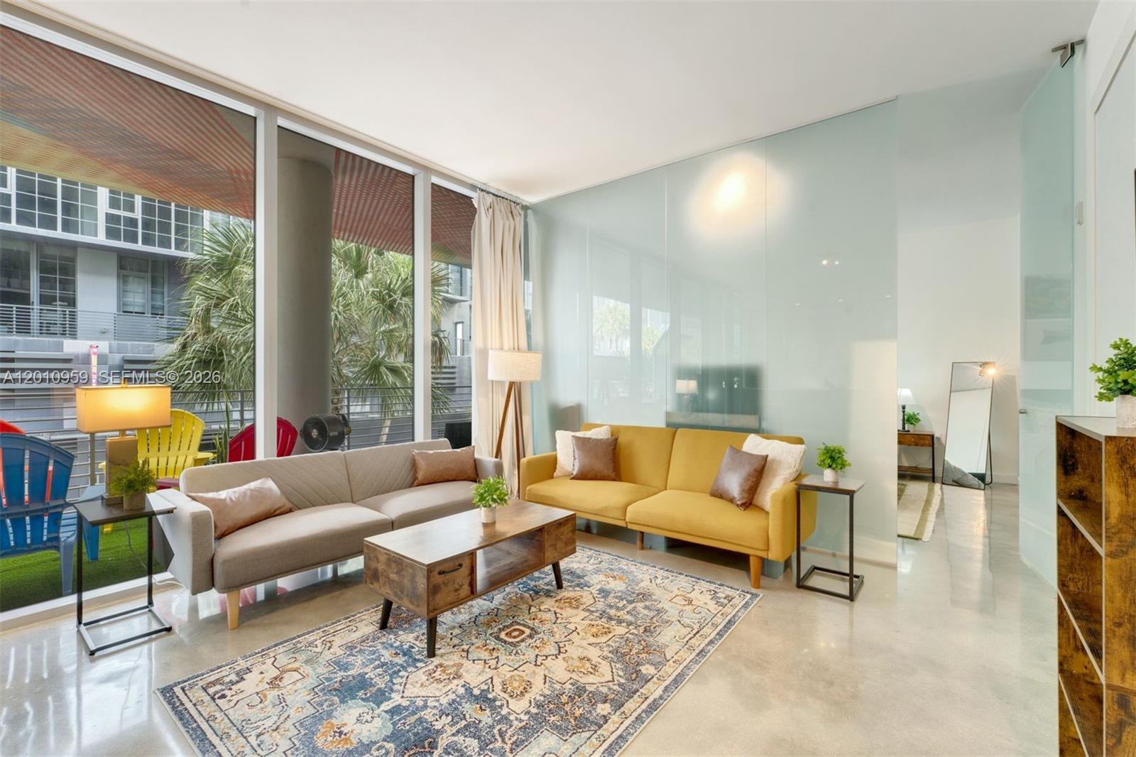 A living room features two sofas, a patterned rug, and floor-to-ceiling windows overlooking a balcony — 250 NW 24th St # 2B, Miami FL 33127, MIAMI, FL