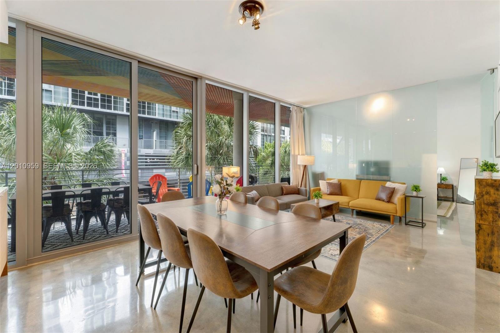 A dining and living area features a wooden table, yellow sofa, and floor-to-ceiling windows — 250 NW 24th St # 2B, Miami FL 33127, MIAMI, FL