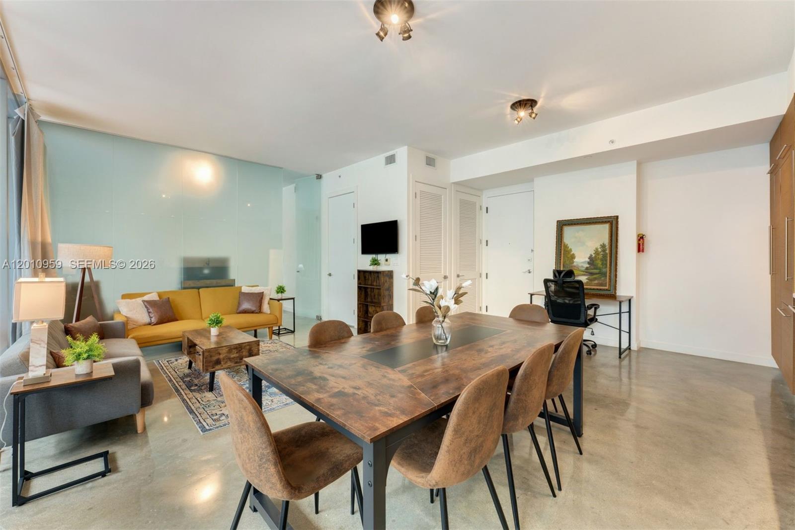 An open-concept living and dining area features concrete floors, a wooden table, and yellow sofa — 250 NW 24th St # 2B, Miami FL 33127, MIAMI, FL