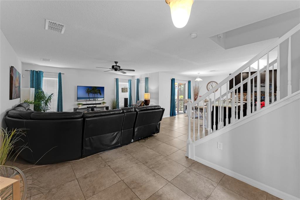 A living room with tile floors, a large black sectional sofa, and a staircase — 2631 SANTOSH COVE, KISSIMMEE, FL