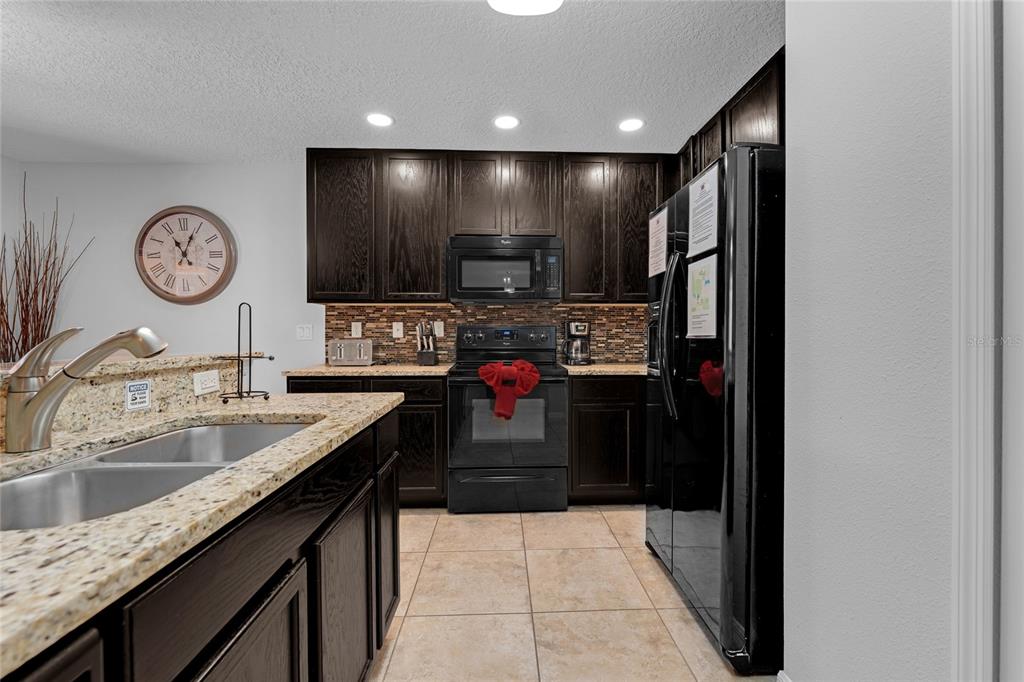 A kitchen features dark wood cabinets, black appliances, granite countertops, and a tiled floor — 2631 SANTOSH COVE, KISSIMMEE, FL
