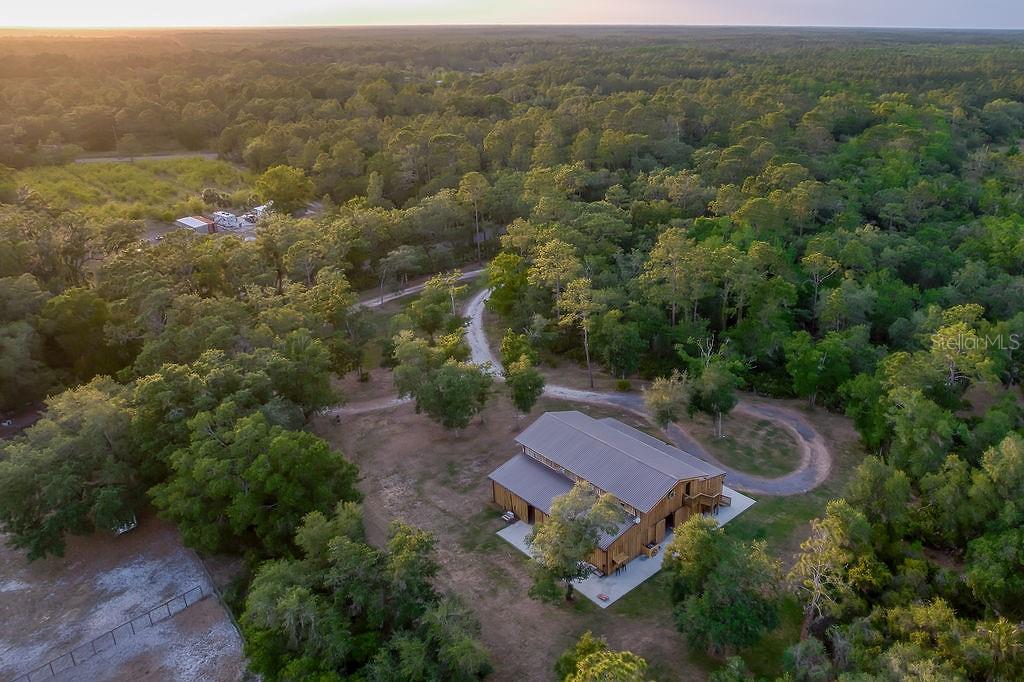 An aerial view shows a wooden barn-style house surrounded by trees and a dirt driveway — 963 LAKE ASHBY ROAD, NEW SMYRNA BEACH, FL