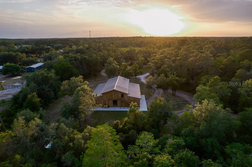 An aerial view shows a wooden barn surrounded by trees at sunset — 963 LAKE ASHBY ROAD, NEW SMYRNA BEACH, FL