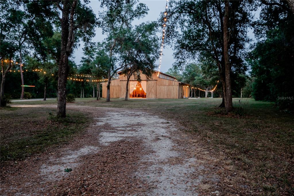 A rustic wooden barn sits at the end of a dirt path under string lights — 963 LAKE ASHBY ROAD, NEW SMYRNA BEACH, FL