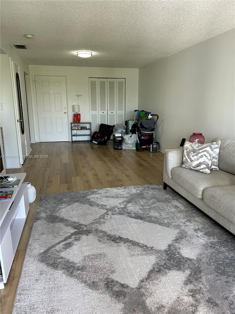 A living room features wood-look flooring, a grey area rug, and a light-colored sofa — 1975 Normandy Dr # 301, Miami Beach FL 33141, MIAMI BEACH, FL