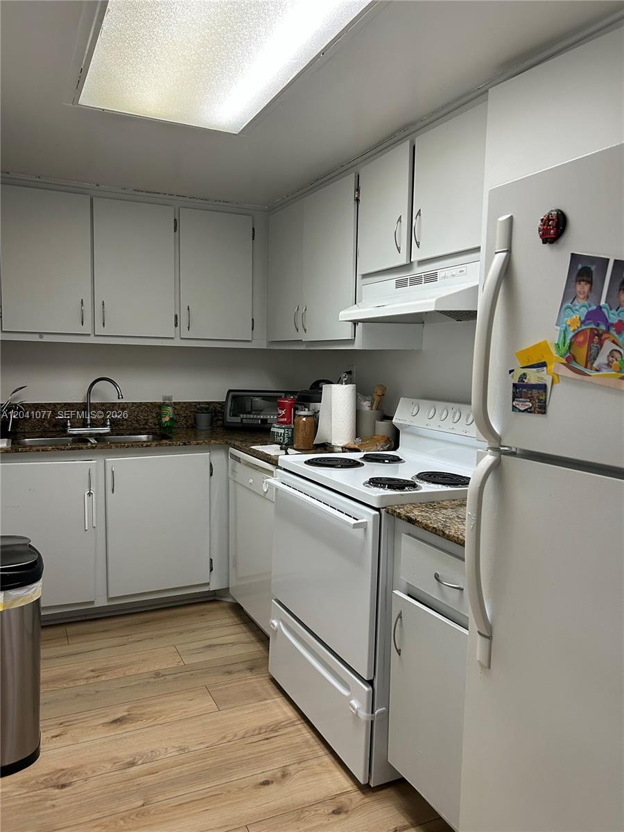 A kitchen features white cabinets, granite countertops, and white appliances on light wood-look flooring — 1975 Normandy Dr # 301, Miami Beach FL 33141, MIAMI BEACH, FL