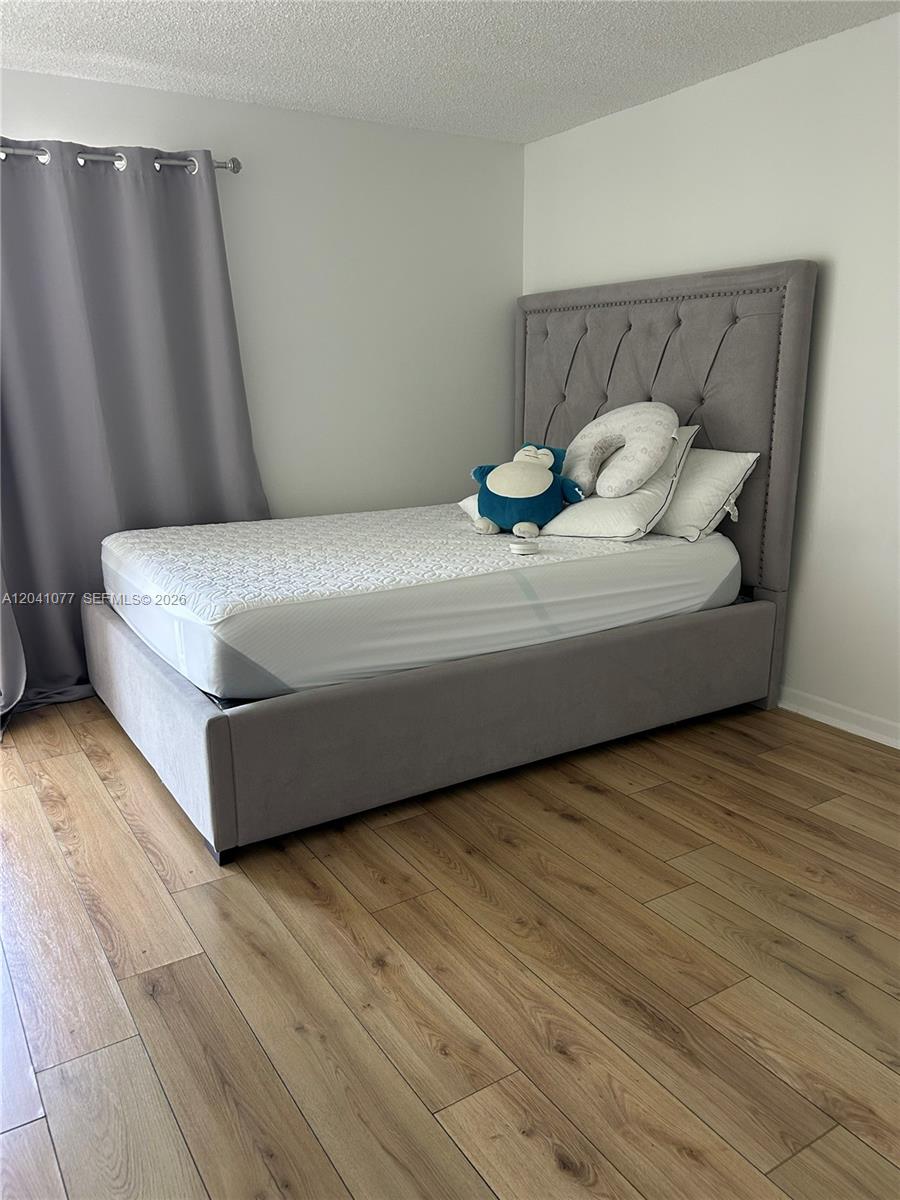 A bedroom features a gray upholstered bed frame, light wood flooring, and gray curtains — 1975 Normandy Dr # 301, Miami Beach FL 33141, MIAMI BEACH, FL