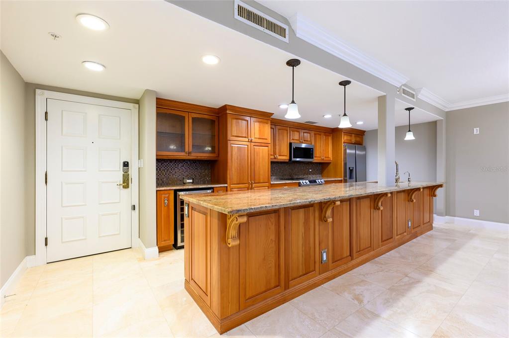 A kitchen features wood cabinetry, a long granite-topped island, and light-colored tile flooring — 36750 US HIGHWAY 19 N UNIT 04221, PALM HARBOR, FL