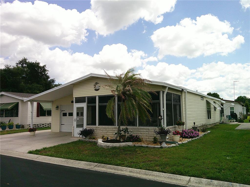 A single-story manufactured home with a screened-in porch, carport, and a palm tree in front — 3120 POND HOLLOW STREET, WESLEY CHAPEL, FL