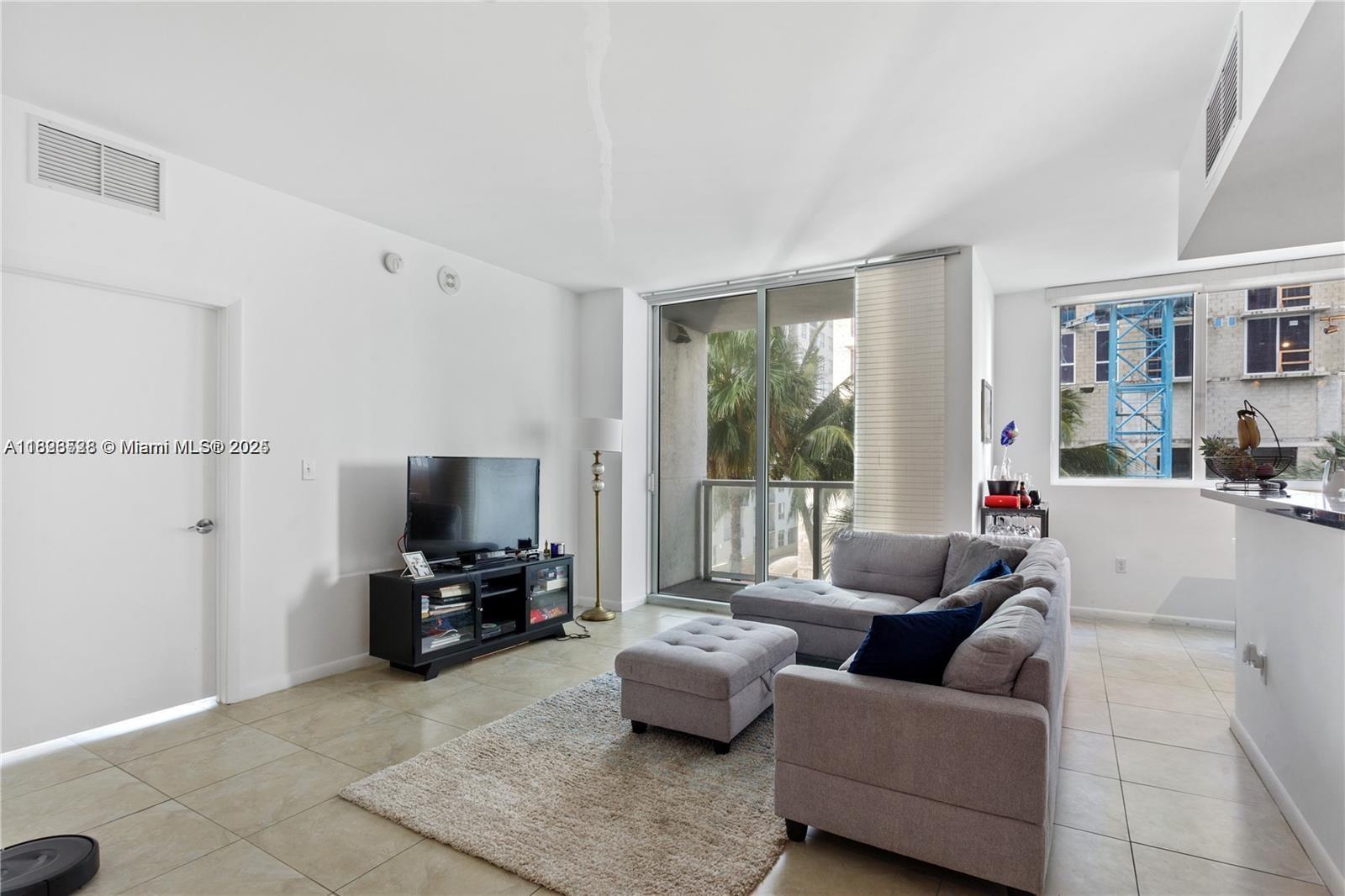 A living room features a grey sectional sofa, a television on a stand, and balcony access — 253 NE 2nd St # 1108, Miami FL 33132, MIAMI, FL
