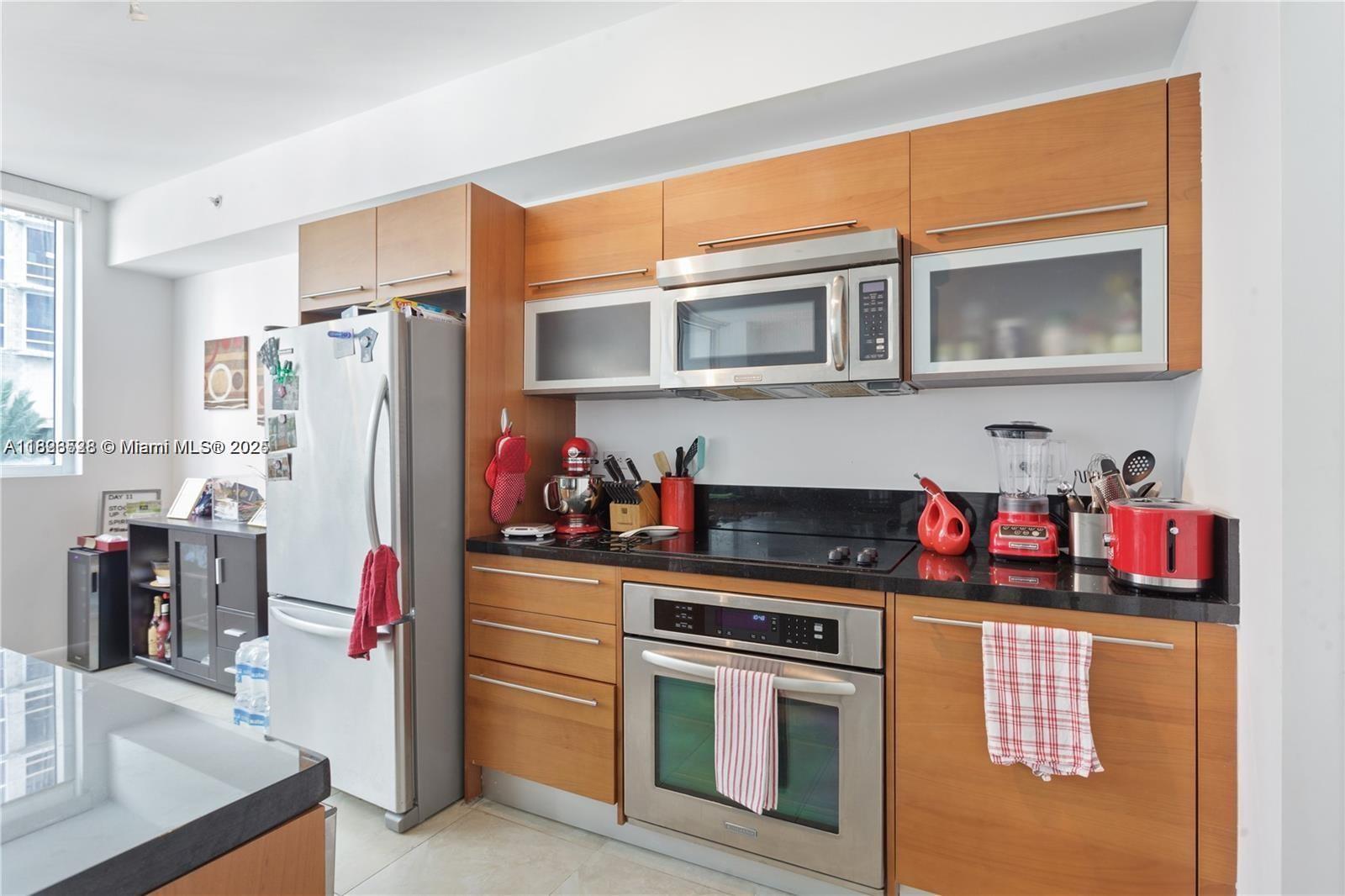 A kitchen features wood cabinets, stainless steel appliances, and black countertops — 253 NE 2nd St # 1108, Miami FL 33132, MIAMI, FL