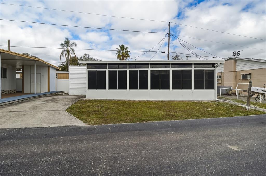 A single-story mobile home features a large, white-framed glass sunroom and an adjacent concrete driveway — 12766 SEMINOLE BOULEVARD UNIT 3, LARGO, FL