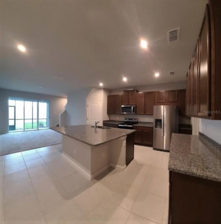 A kitchen with dark wood cabinets, granite countertops, a center island, and stainless steel appliances — 2525 ARBOR WIND DRIVE, LUTZ, FL