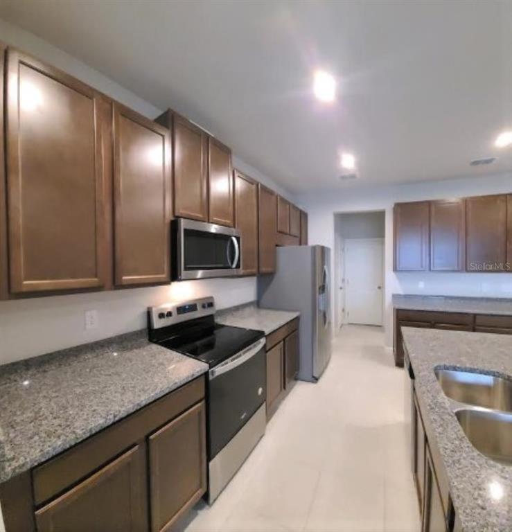 A kitchen features dark wood cabinets, granite countertops, stainless steel appliances, and tile flooring — 2525 ARBOR WIND DRIVE, LUTZ, FL