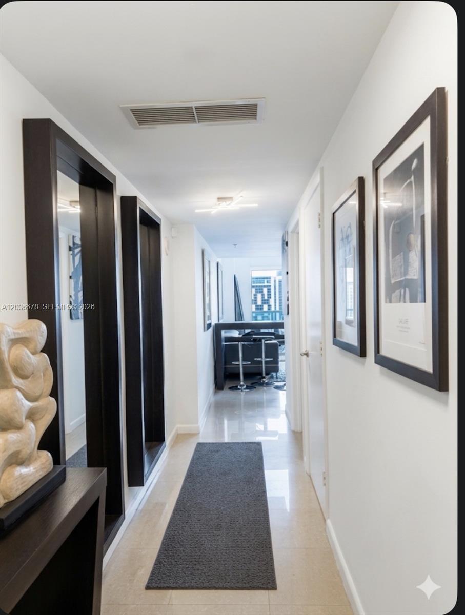 A hallway with white walls, dark-framed mirrors, framed artwork, and a gray runner rug — MIAMI, FL