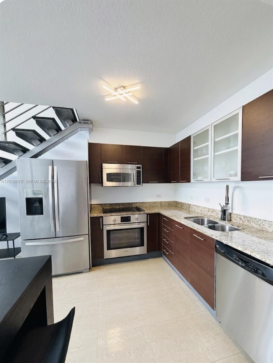 A kitchen features dark wood cabinets, granite countertops, stainless steel appliances, and an adjacent staircase — MIAMI, FL