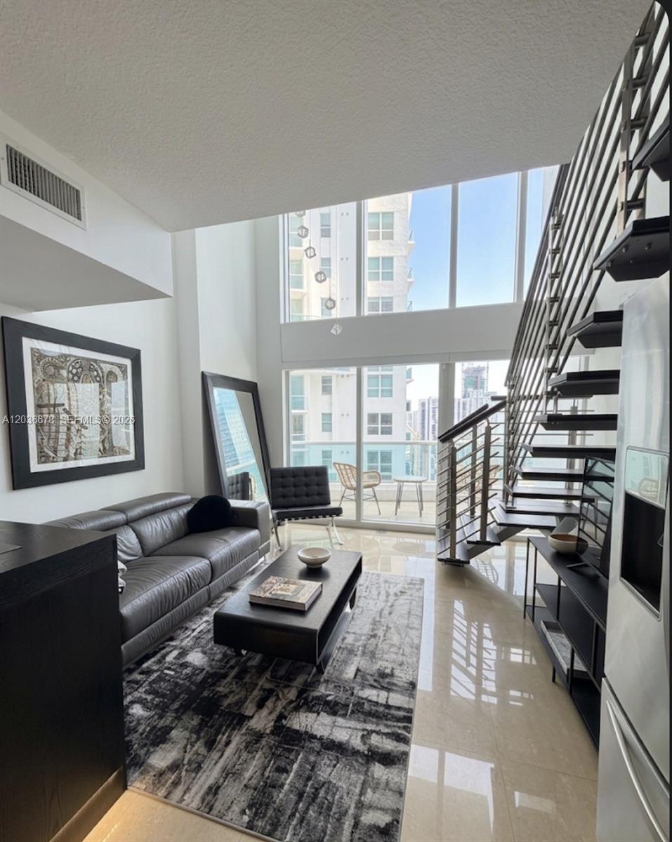 A modern living room features a leather sofa, a floating staircase, and floor-to-ceiling windows — MIAMI, FL