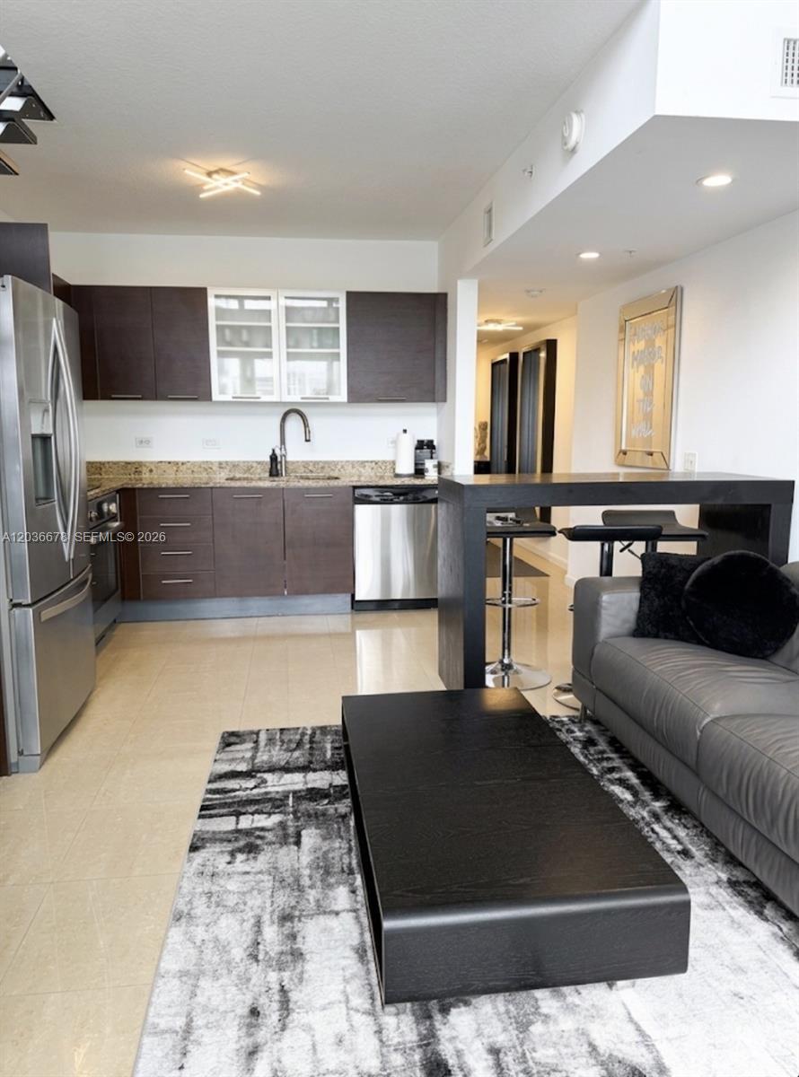 A modern kitchen with dark cabinetry and stainless steel appliances opens into a living area — MIAMI, FL