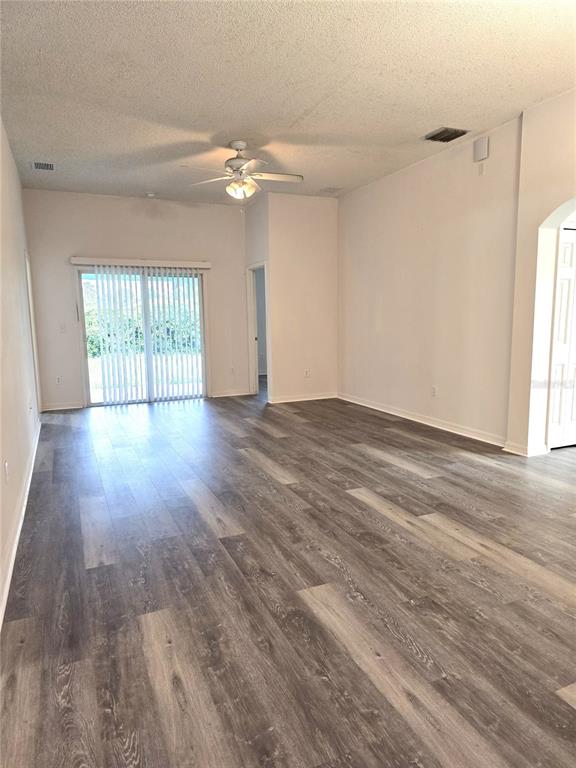 An empty living room features wood-look flooring, a ceiling fan, and sliding glass patio doors — 11010 WHITECAP DRIVE, RIVERVIEW, FL