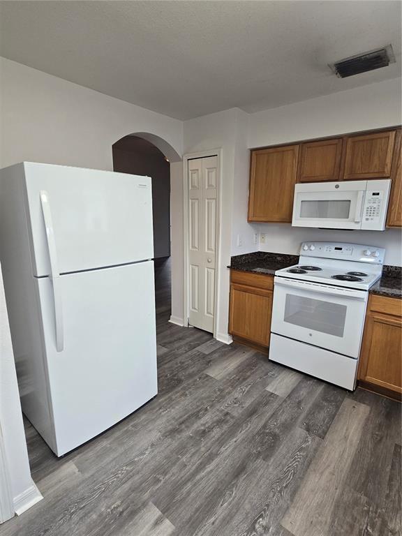 A kitchen features wood cabinets, white appliances, dark countertops, and gray wood-look flooring — 11010 WHITECAP DRIVE, RIVERVIEW, FL
