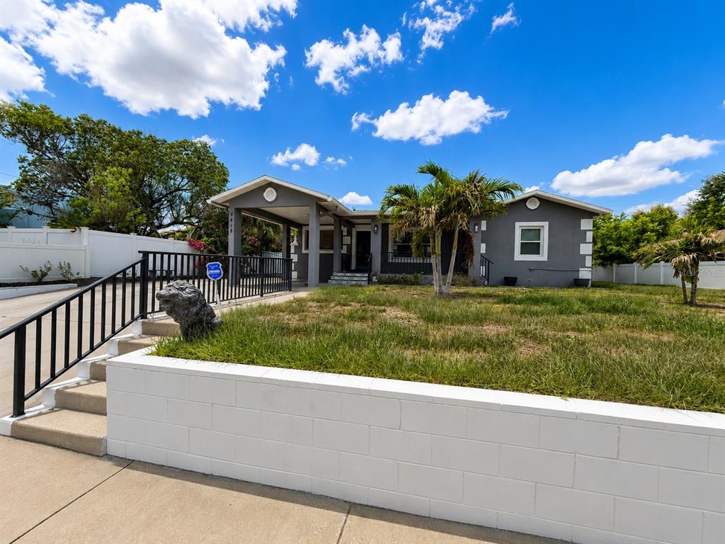 A gray single-story house features a covered entryway, a white block retaining wall, and landscaping — 3815 W NORTH B STREET, TAMPA, FL