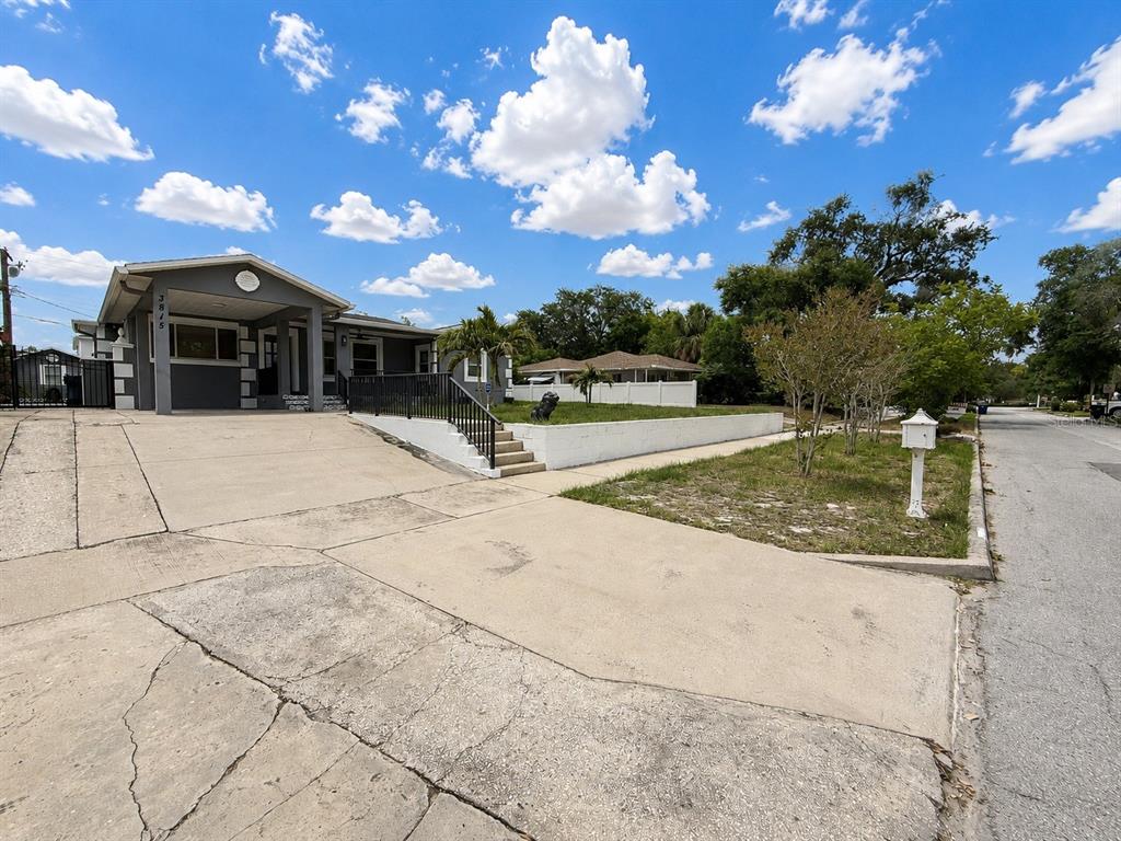 A gray house with a concrete driveway and a raised yard behind a retaining wall — 3815 W NORTH B STREET, TAMPA, FL