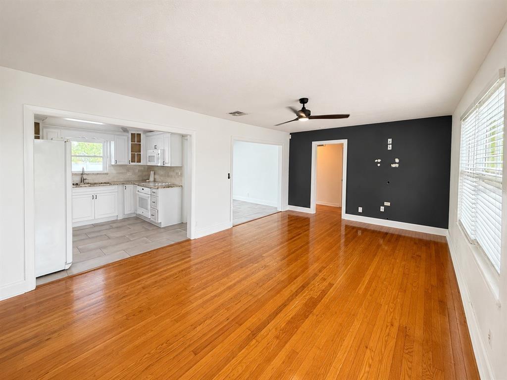A living room with hardwood floors, a dark accent wall, and an adjacent white kitchen — 3815 W NORTH B STREET, TAMPA, FL