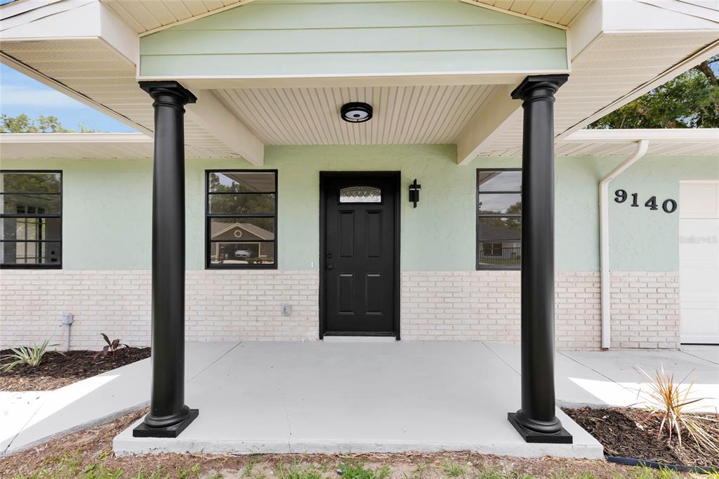 A covered front porch features two black columns, a black front door, and light-colored siding — 9140 SE 155TH PLACE, SUMMERFIELD, FL