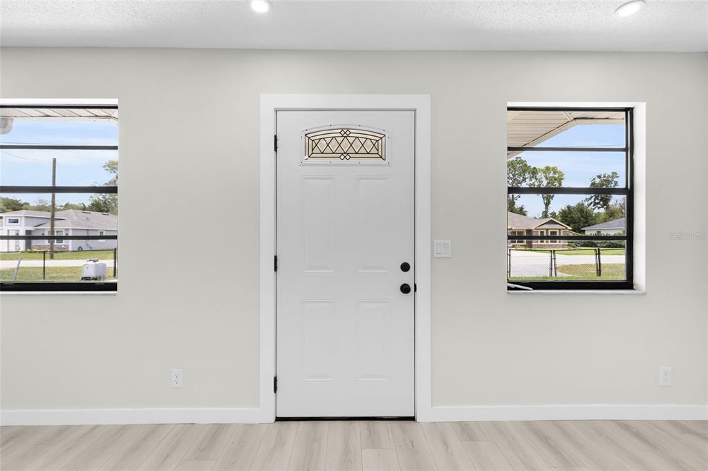 A white front door is centered between two windows in a room with light flooring — 9140 SE 155TH PLACE, SUMMERFIELD, FL