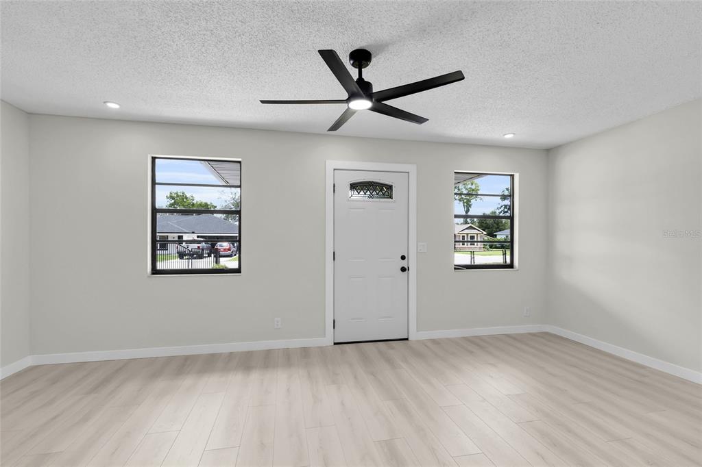 A room with light-colored walls, wood-look flooring, a ceiling fan, and a white front door — 9140 SE 155TH PLACE, SUMMERFIELD, FL