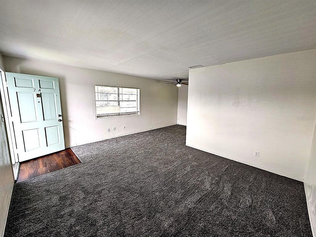 An empty living room features gray carpeting, white walls, and a light blue front door — 5924 5TH AVENUE N UNIT A7, ST PETERSBURG, FL