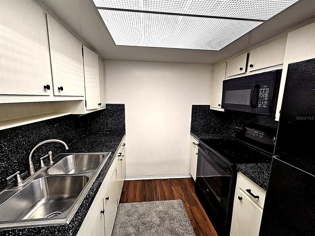 A galley kitchen features white cabinets, black speckled countertops, stainless steel sink, and black appliances — 5924 5TH AVENUE N UNIT A7, ST PETERSBURG, FL