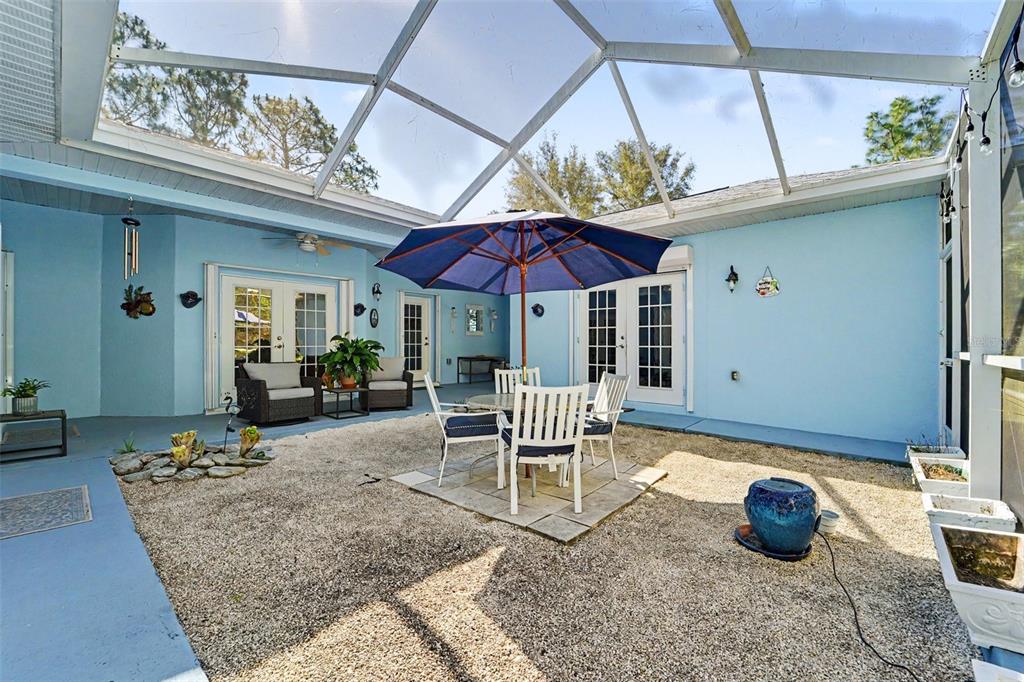 A screened-in patio features a gravel floor, a dining set with an umbrella, and blue walls — 5432 N PECOS TERRACE, BEVERLY HILLS, FL