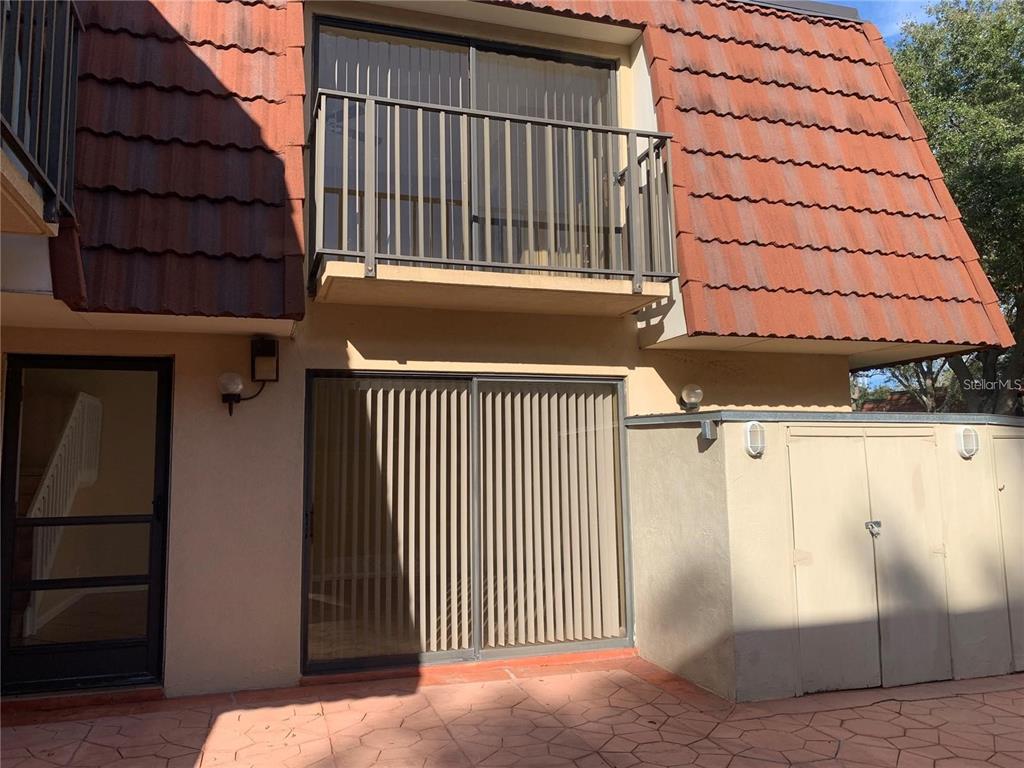 A two-story building exterior features a ground-level patio, sliding glass doors, and an upper balcony — 2602 7TH COURT UNIT 15, PALM HARBOR, FL
