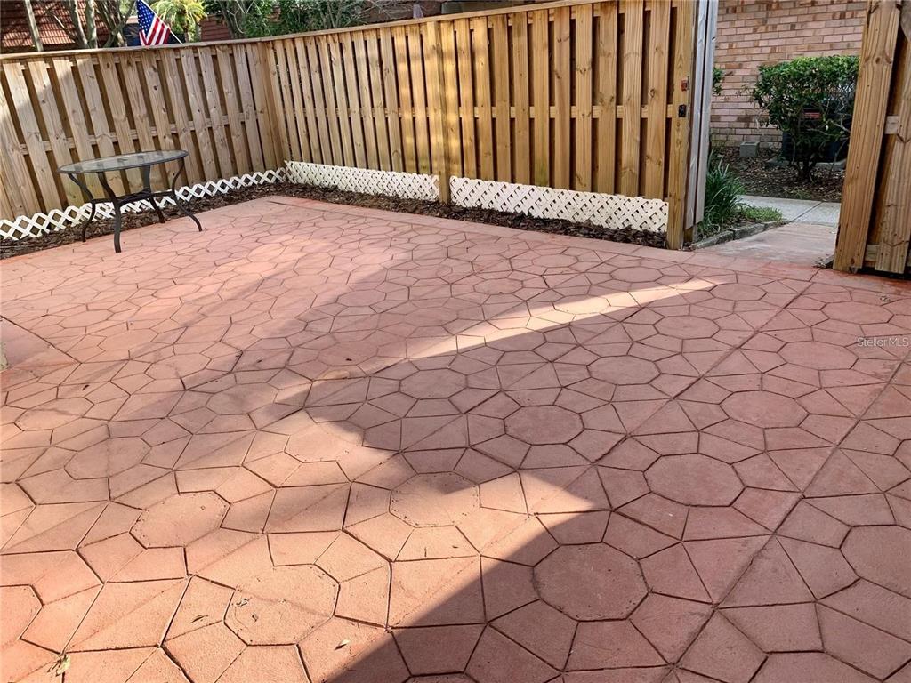 A fenced-in patio features patterned red concrete pavers and a small glass-topped table — 2602 7TH COURT UNIT 15, PALM HARBOR, FL