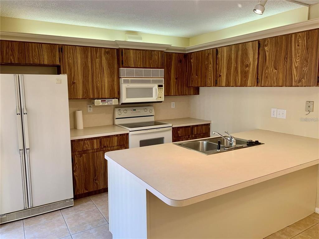 A kitchen features wood-grain cabinets, white appliances, a central island with a sink, and tile flooring — 2602 7TH COURT UNIT 15, PALM HARBOR, FL