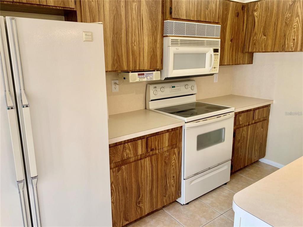 A kitchen features wood-grain cabinets, white appliances, and beige countertops — 2602 7TH COURT UNIT 15, PALM HARBOR, FL
