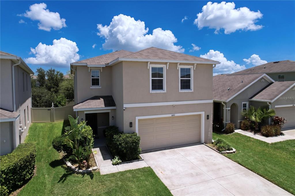A two-story beige house with a two-car garage and a front lawn under a blue sky — 16192 SILENT SANDS LANE, ODESSA, FL