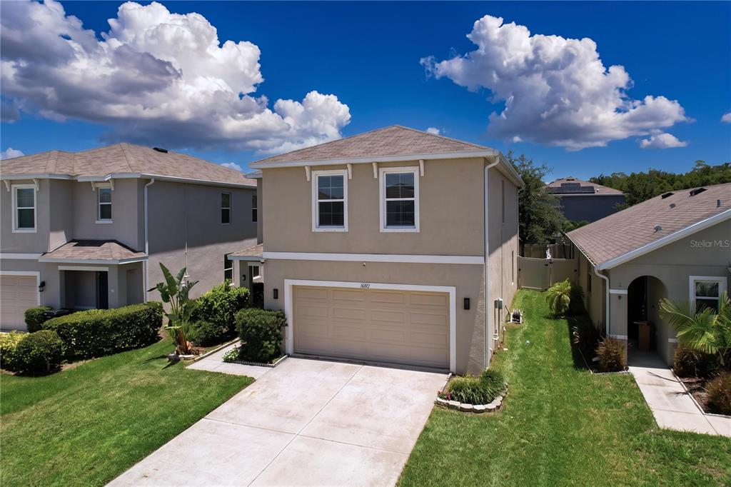An exterior view of a two-story beige house with a two-car garage and lawn — 16192 SILENT SANDS LANE, ODESSA, FL