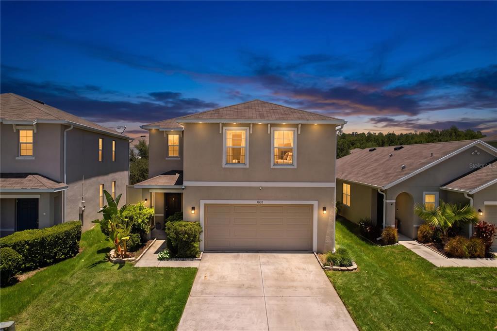 A two-story suburban house with a beige stucco exterior and a two-car garage at dusk — 16192 SILENT SANDS LANE, ODESSA, FL