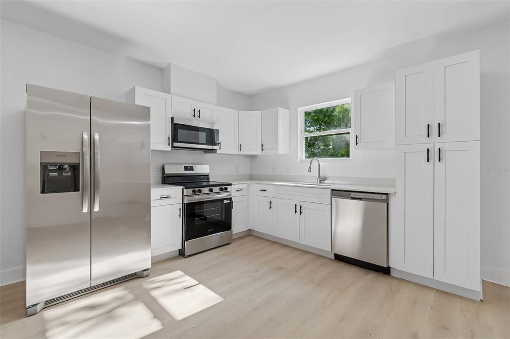 A kitchen features white cabinets, stainless steel appliances, and light wood-look flooring — 2021 AVA CIRCLE, BARTOW, FL