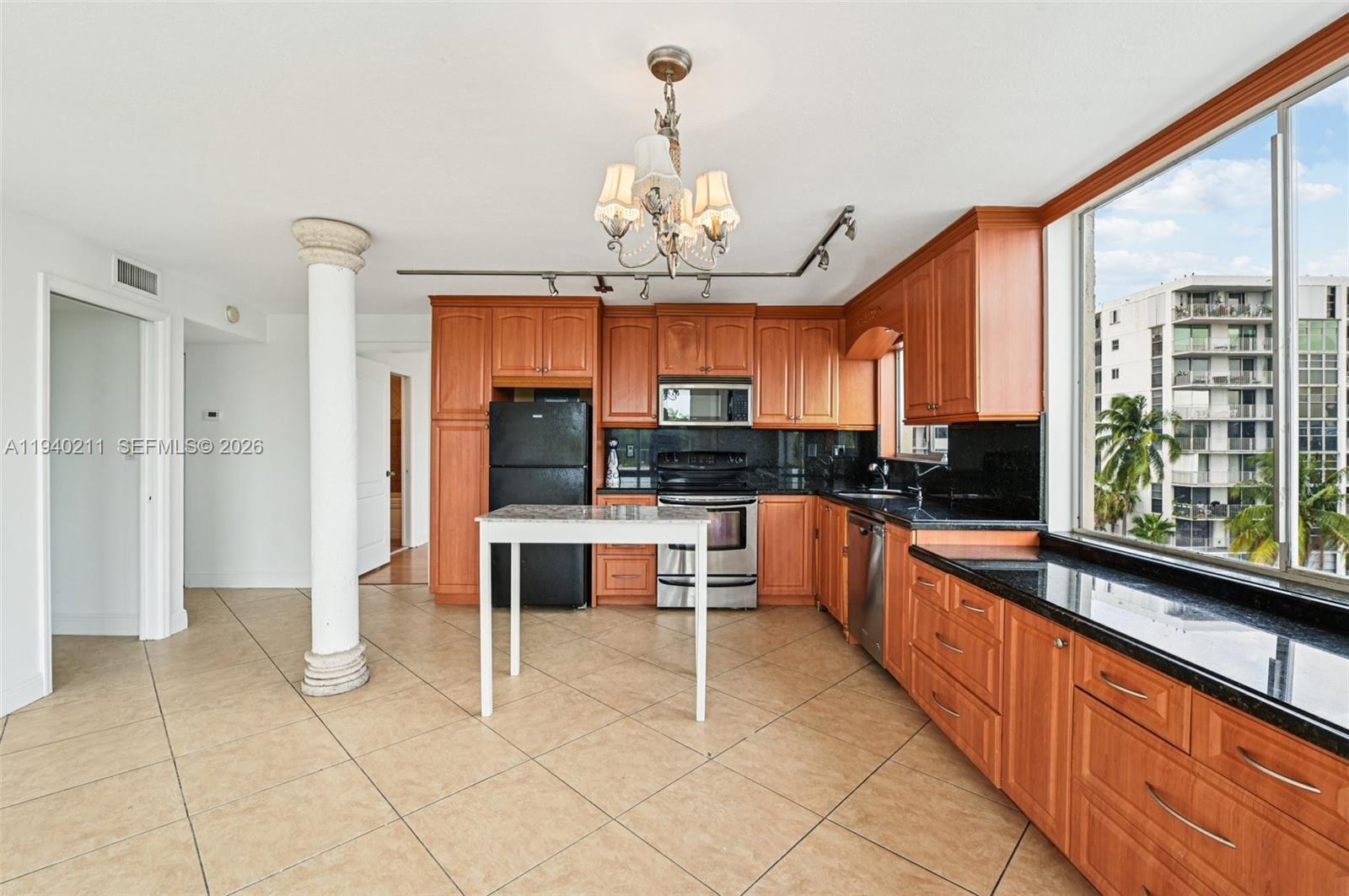 A kitchen features wood cabinets, black countertops, stainless steel appliances, and a central white table — 1740 NW N River Dr # 614, Miami FL 33125, MIAMI, FL