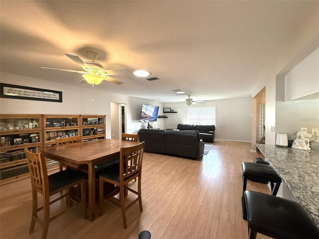 An open-concept living and dining area features light wood flooring, ceiling fans, and granite countertops — 3604 E ONYX PLACE, HERNANDO, FL