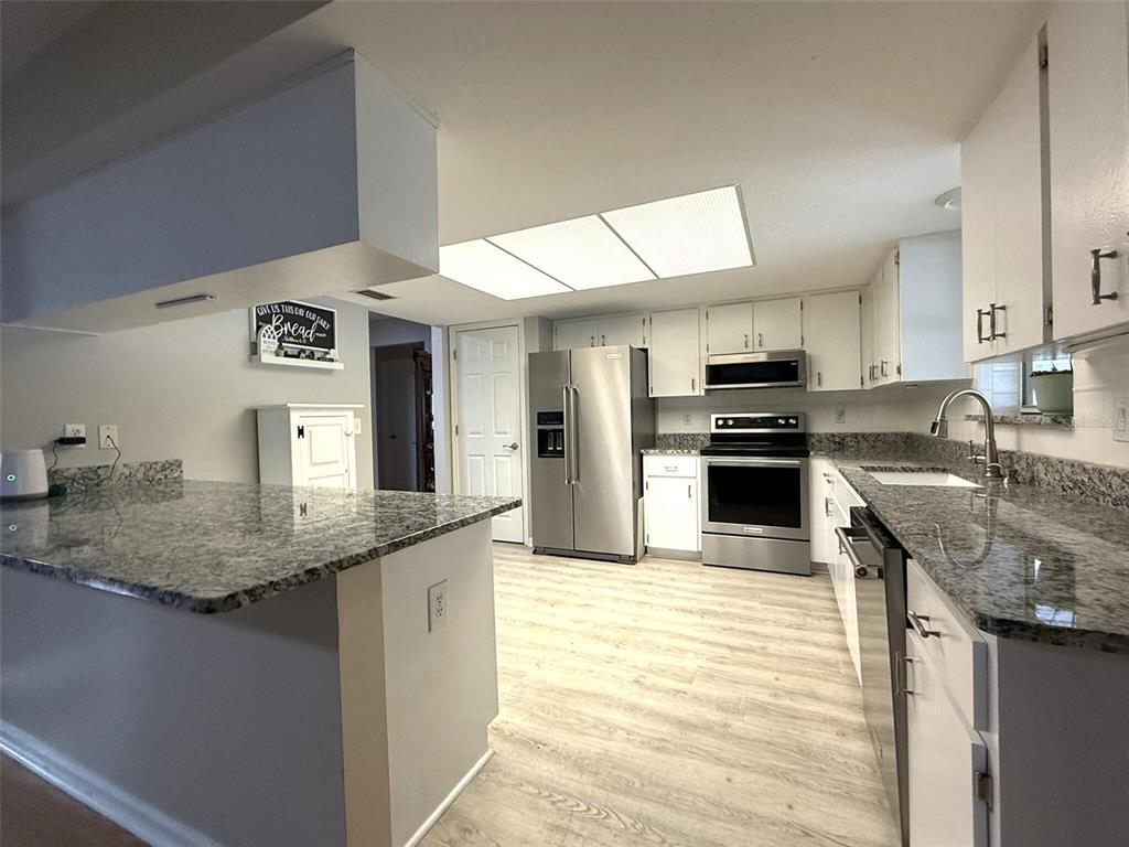 A kitchen features white cabinets, granite countertops, stainless steel appliances, and light wood-look flooring — 3604 E ONYX PLACE, HERNANDO, FL