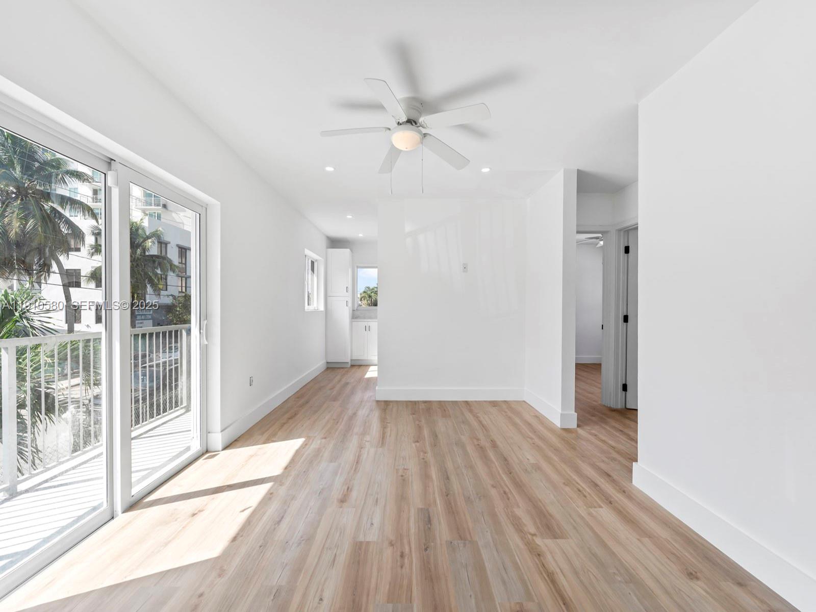 A bright, minimalist living area features light wood-look flooring, a ceiling fan, and balcony access — 300 NW 7th Ave # 1, Miami FL 33128, MIAMI, FL
