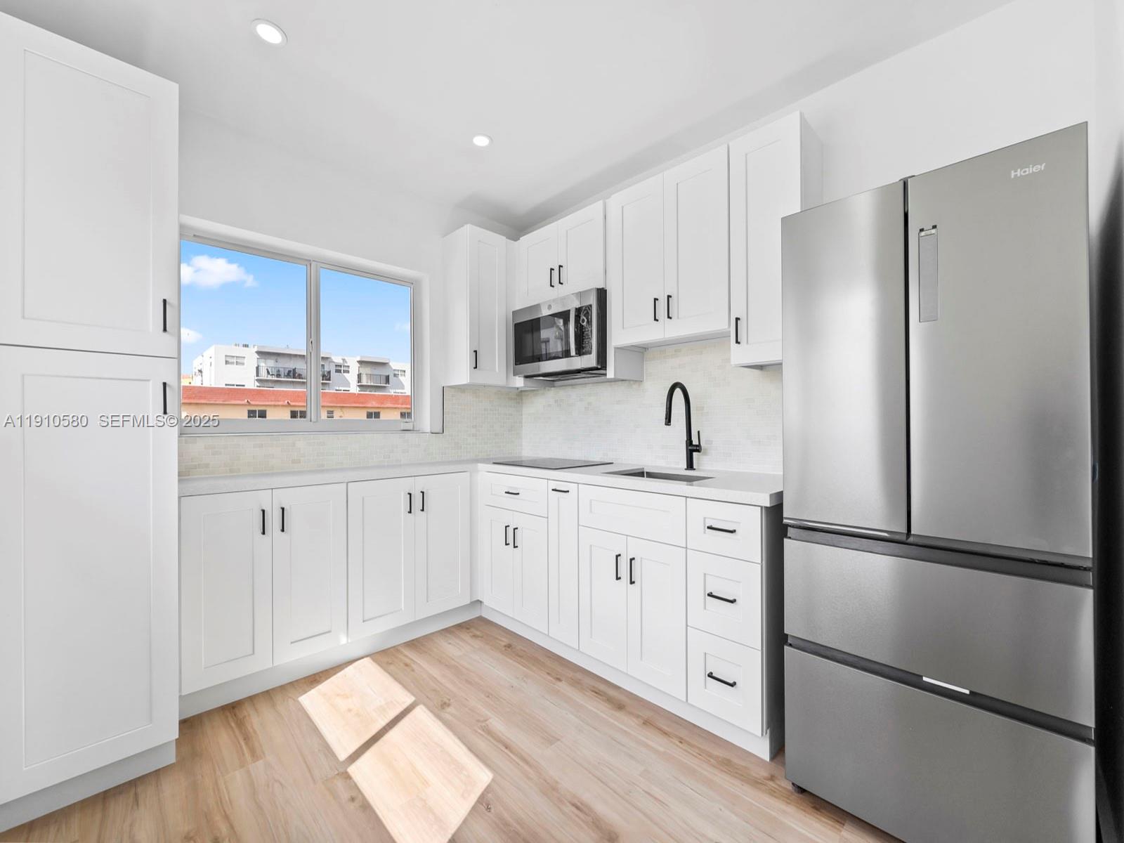 A modern kitchen features white cabinets, stainless steel appliances, and light wood-look flooring — 300 NW 7th Ave # 1, Miami FL 33128, MIAMI, FL