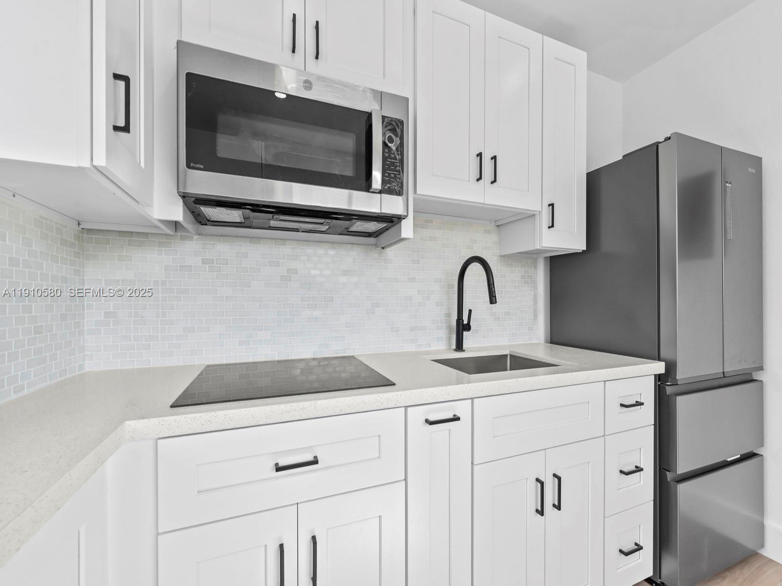 A modern kitchen features white cabinets, stainless steel appliances, a tiled backsplash, and quartz countertops — 300 NW 7th Ave # 1, Miami FL 33128, MIAMI, FL