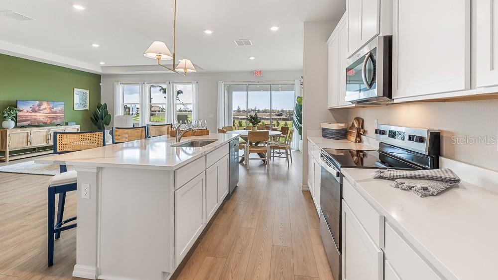 A modern kitchen features white cabinets, quartz countertops, and an island overlooking an open living area — 10649 FERN HOLLOW RUN, PARRISH, FL