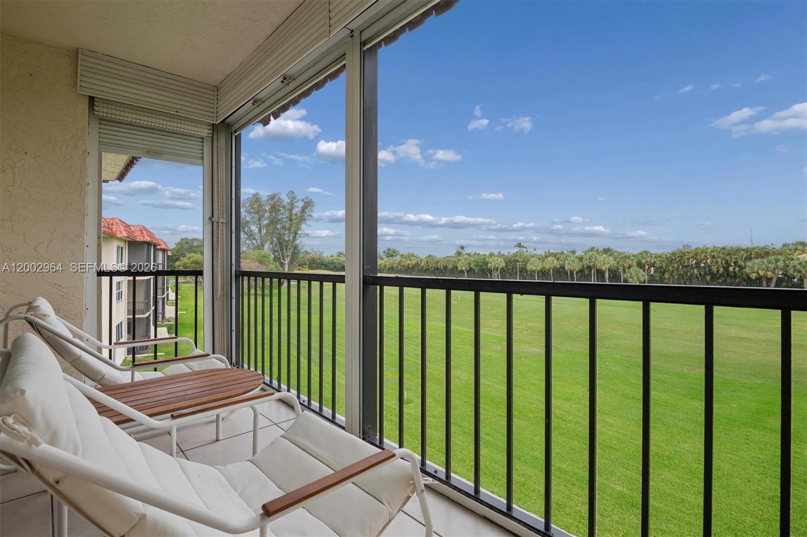 A screened balcony features white lounge chairs and a view of a grassy field — PEMBROKE PINES, FL